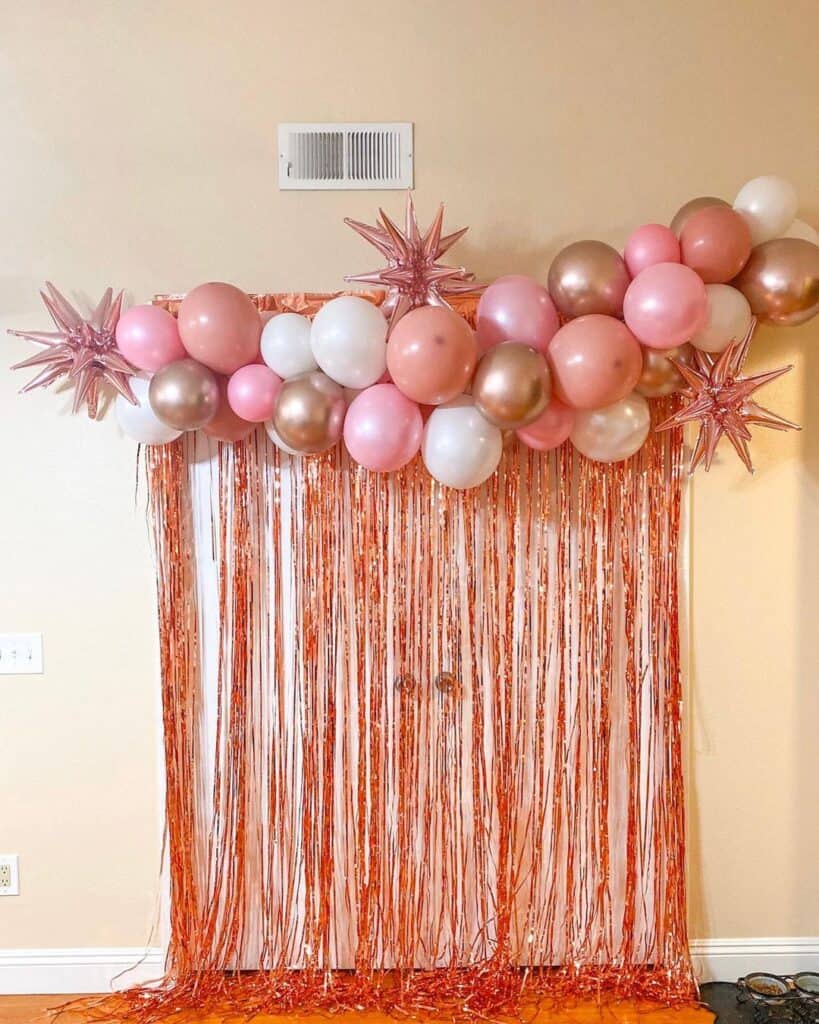 Rose gold graduation party backdrop consists of rose gold and white balloons and rose gold shinny tassels.